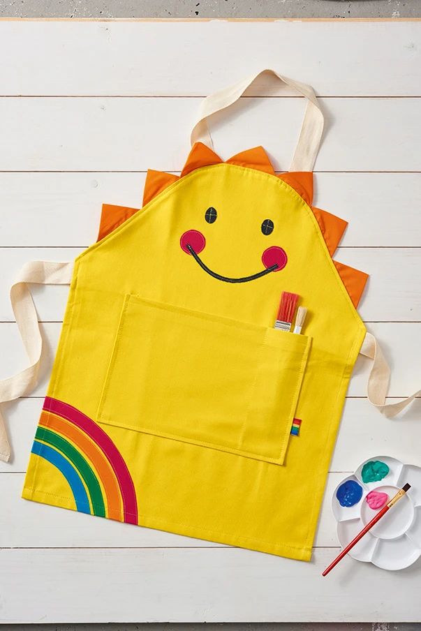 a child's apron with a smiling face on it and paintbrushes next to it