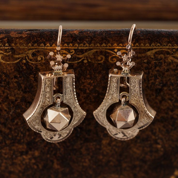 Antique Victorian Dangle Earrings in 14k Yellow Gold These 14 karat yellow gold drop dangle earrings are over 130 years old and have remained a pair!  The tear drop geometric shape and swinging multi-sided geometric gold ball in the center helps create movement and design interest. These Victorian earring also feature hand engraving with a delicate scalloped edge.  The 14 karat yellow gold Shepard's hook wire with safety catch will ensure that the earring will be together for an additional 130 y Antique 14k Gold Hallmarked Earrings, Formal Engraved Drop Earrings, Yellow Gold Engraved Drop Earrings, Engraved Yellow Gold Drop Earrings, Victorian Yellow Gold Dangle Earrings, Elegant Engraved Dangle Earrings, Heirloom Pierced Drop Earrings, Heirloom Drop Earrings, Pierced, Heirloom Drop Earrings