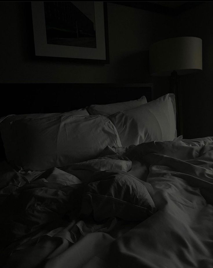 an unmade bed in a dark room with white sheets and pillows on top of it