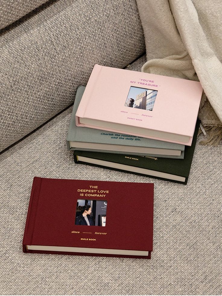 a stack of books sitting on top of a couch next to a pillow and blanket