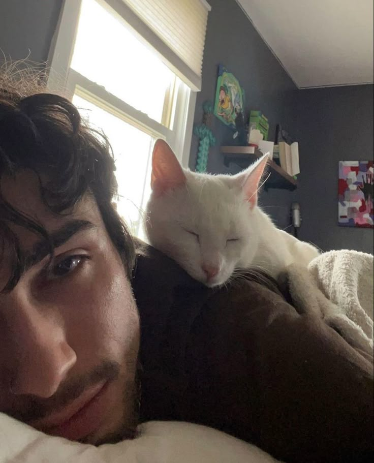 a man laying on top of a bed with a white cat sleeping next to him