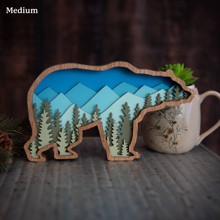 a bear shaped wooden cutout sitting next to a coffee cup and pine tree decoration