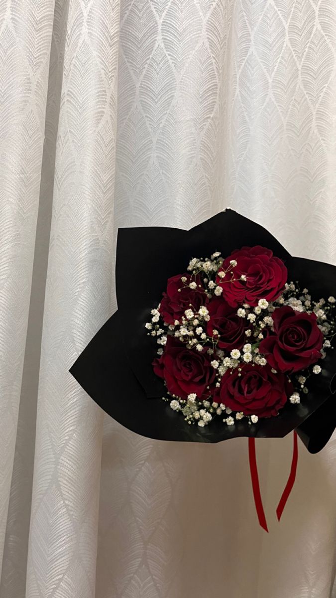 a bouquet of red roses in a black paper hat with baby's breath and baby's breath