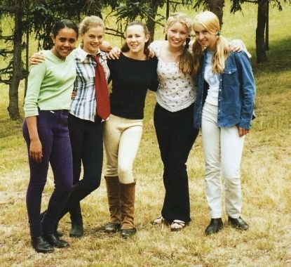 a group of young women standing next to each other on a grass covered field with trees in the background