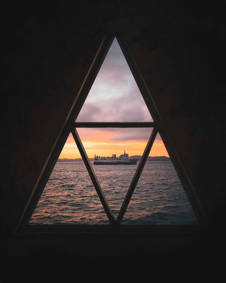 a window with a view of the ocean and a ship in the distance at sunset