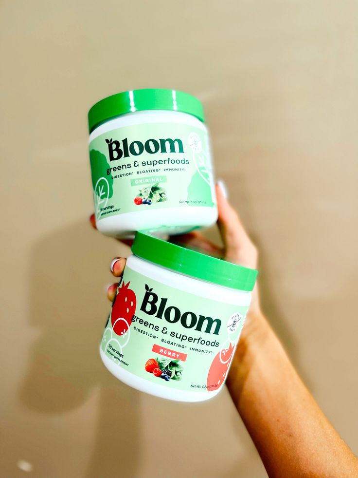 two jars of bloom are being held up by someone's hand in front of a wall