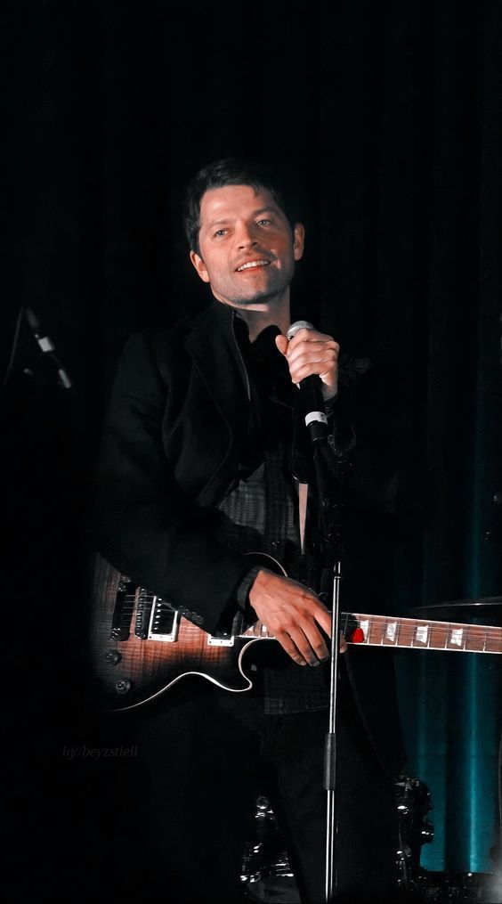 a man holding a guitar while standing in front of a microphone and singing into a microphone