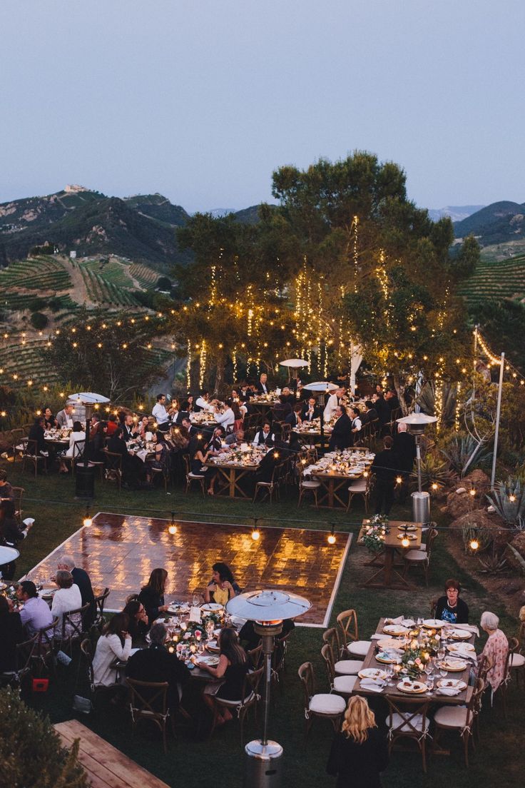 a group of people sitting at tables in the middle of a field with lights on them