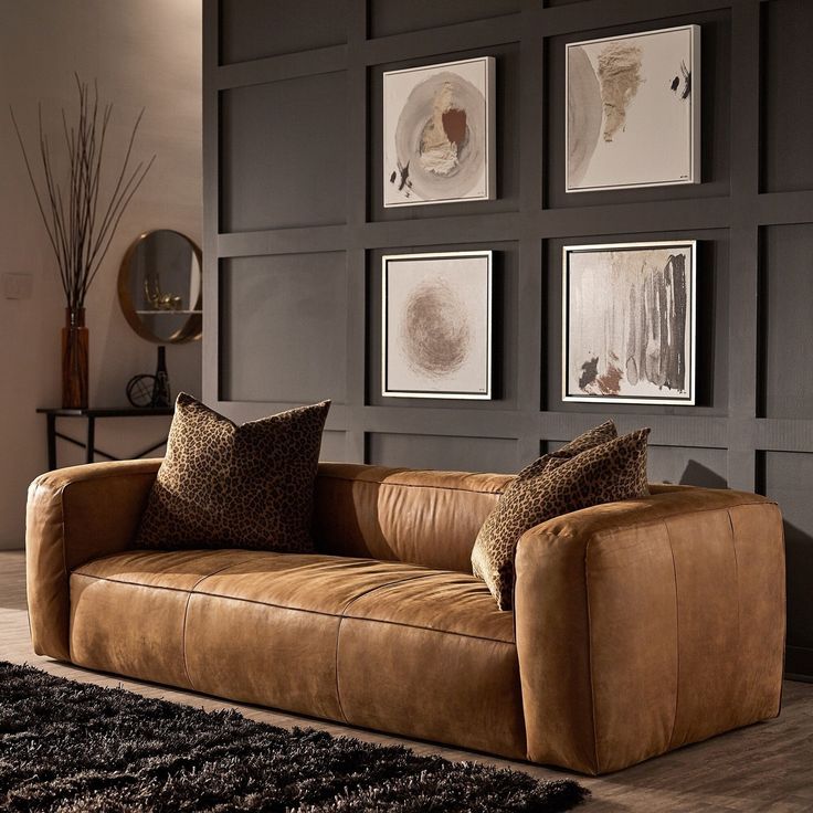 a brown couch sitting in front of two framed pictures on a wall next to a rug