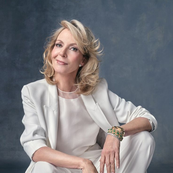 a woman sitting on top of a chair wearing a white suit and holding her hands together