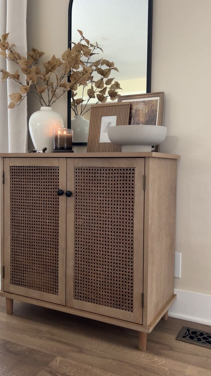 a wooden cabinet sitting on top of a hard wood floor next to a vase filled with flowers