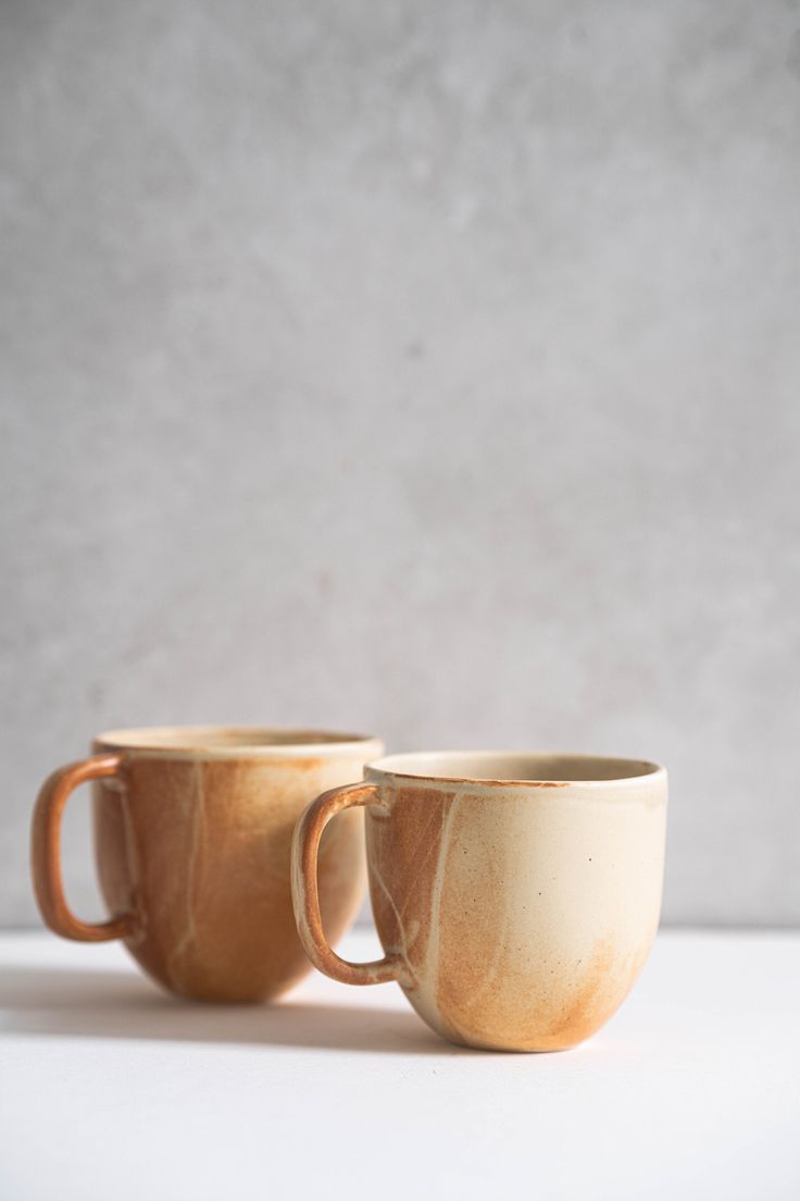 two coffee mugs sitting side by side on a white countertop, one has a brown handle