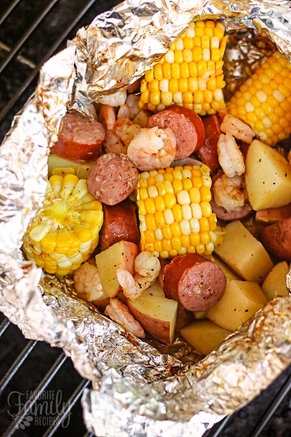 corn on the cob with sausage and potatoes in foil wrapped over an open grill