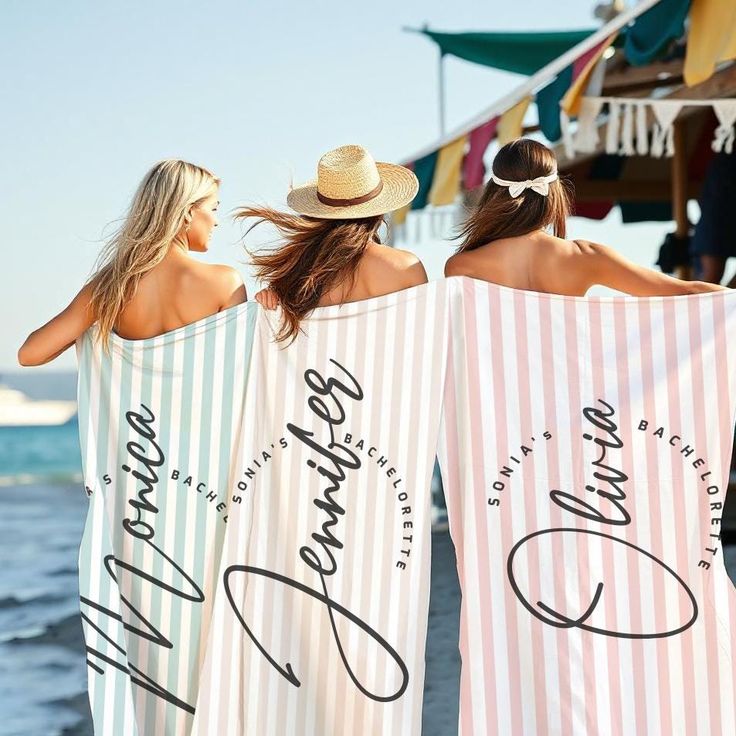 two women in matching towels on the beach with their backs to each other and one holding her hair back