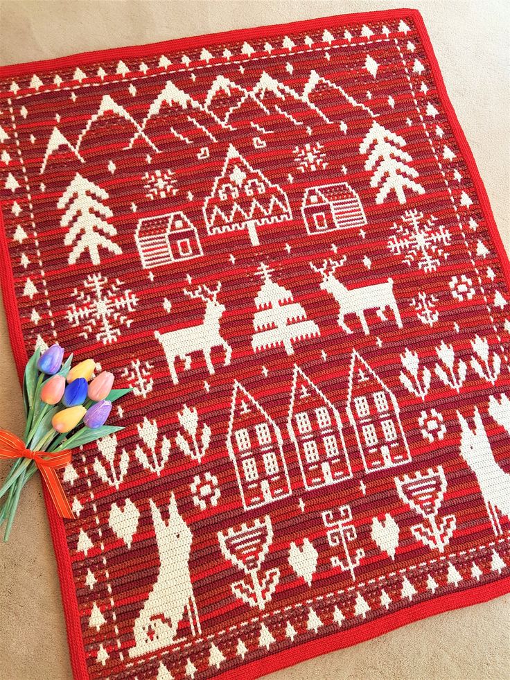 a red and white knitted placemat with houses, trees, deers and snowflakes