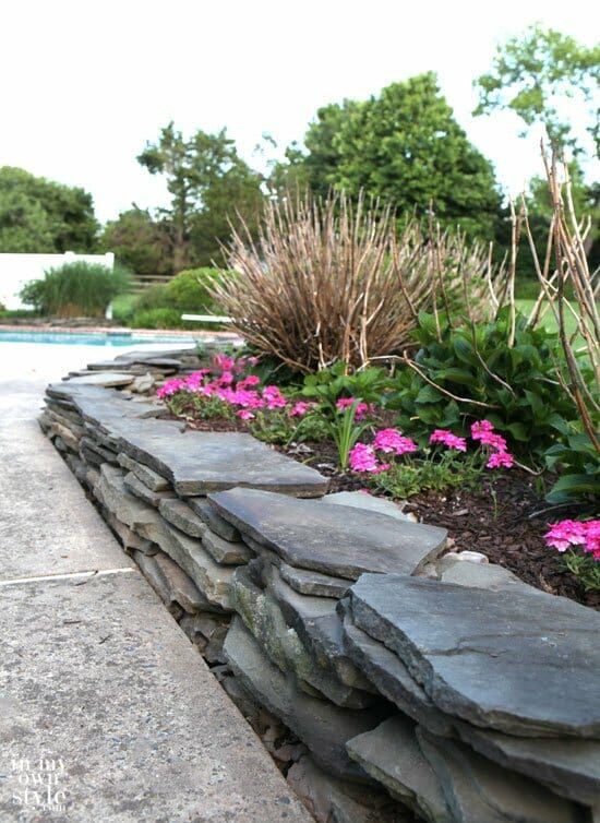 a stone wall with pink flowers in the foreground