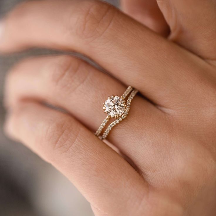 a woman's hand with a diamond ring on top of her finger and the other hand holding an engagement ring