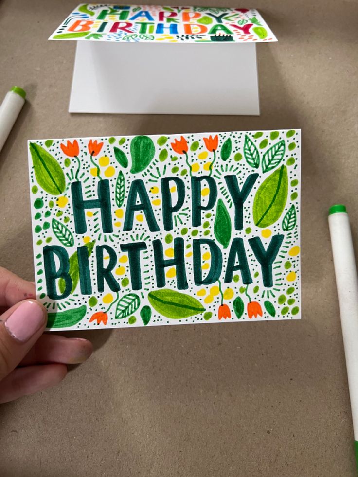 someone holding up a card with the words happy birthday written in green and orange on it