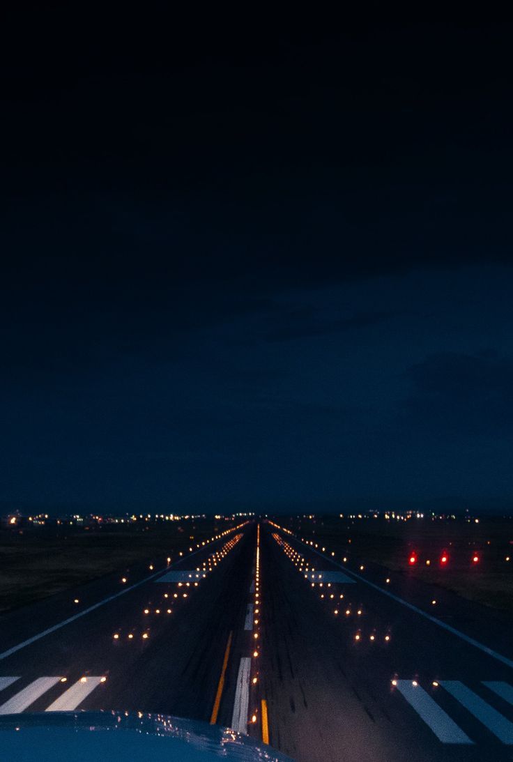 an airport runway at night with lights on the tarmac and cars driving down it