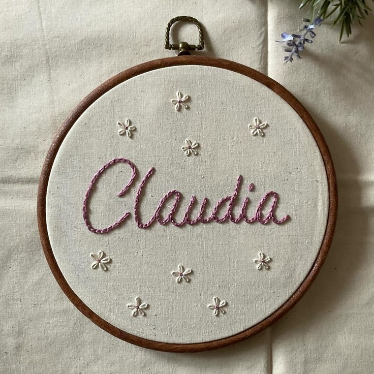 embroidered hoop with the word claudia written in pink and white letters on it, surrounded by flowers