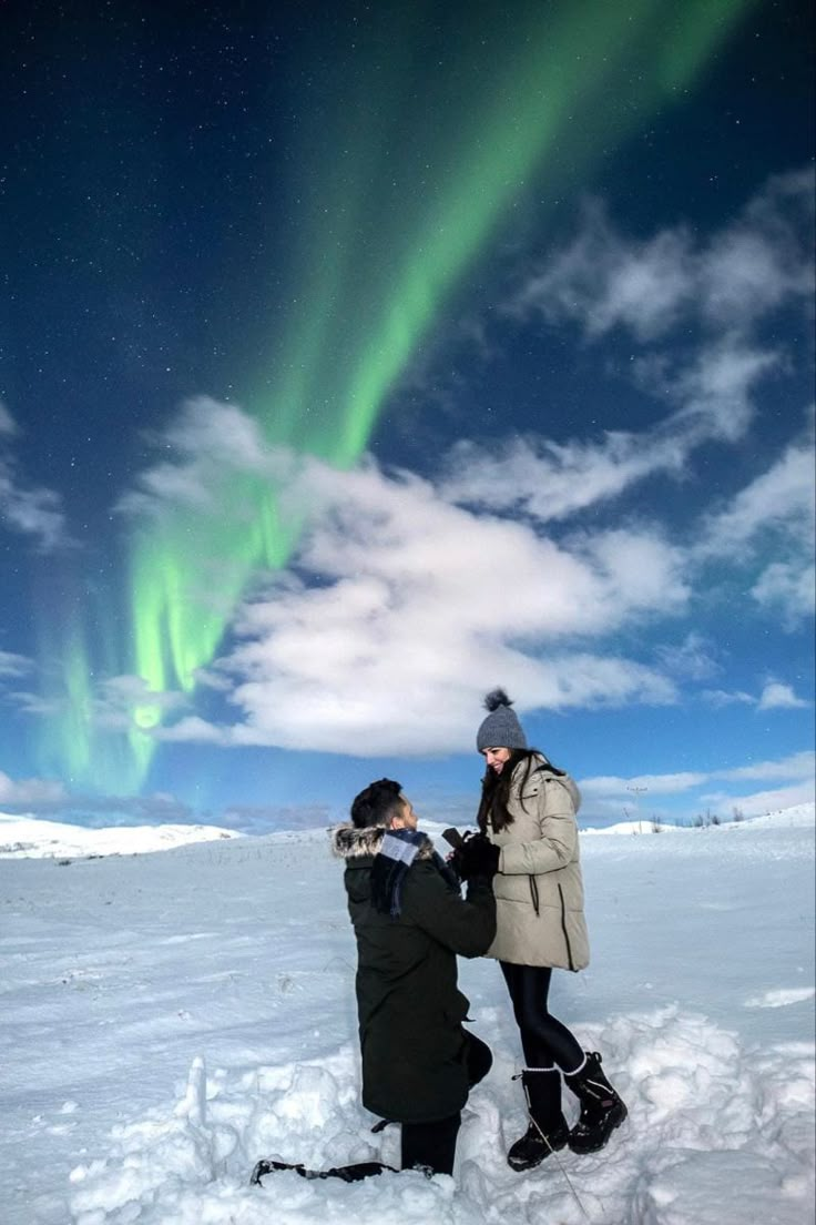 two people are standing in the snow with an aurora bore above them and looking at something