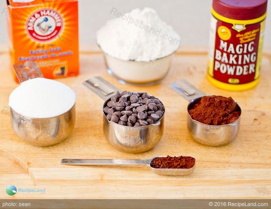 ingredients to make chocolate cake sitting on a cutting board with measuring cups and spoons