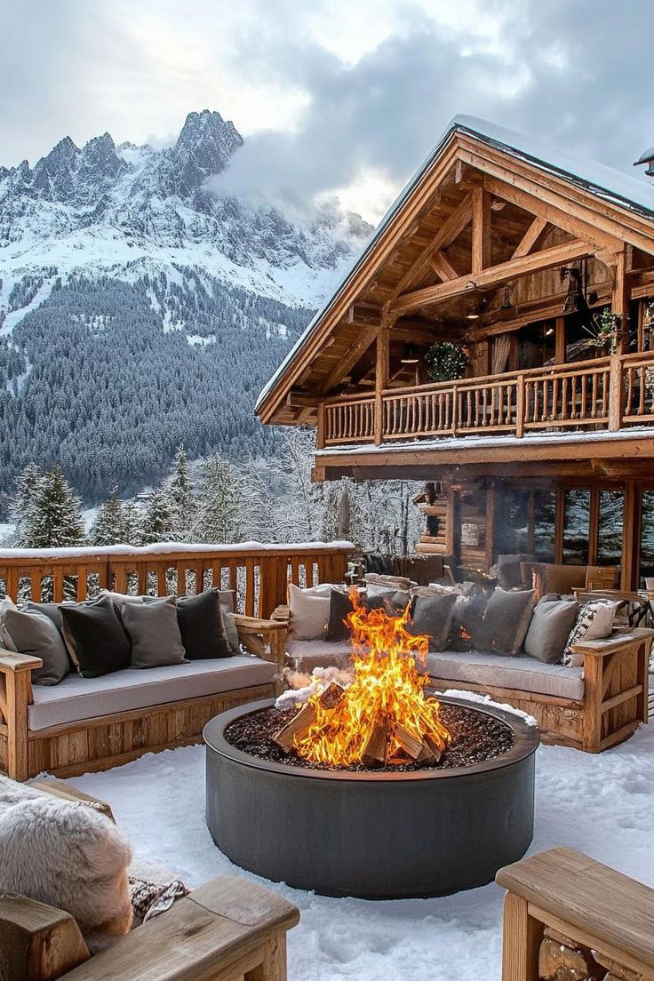 an outdoor fire pit in the middle of snow covered ground with mountains in the background