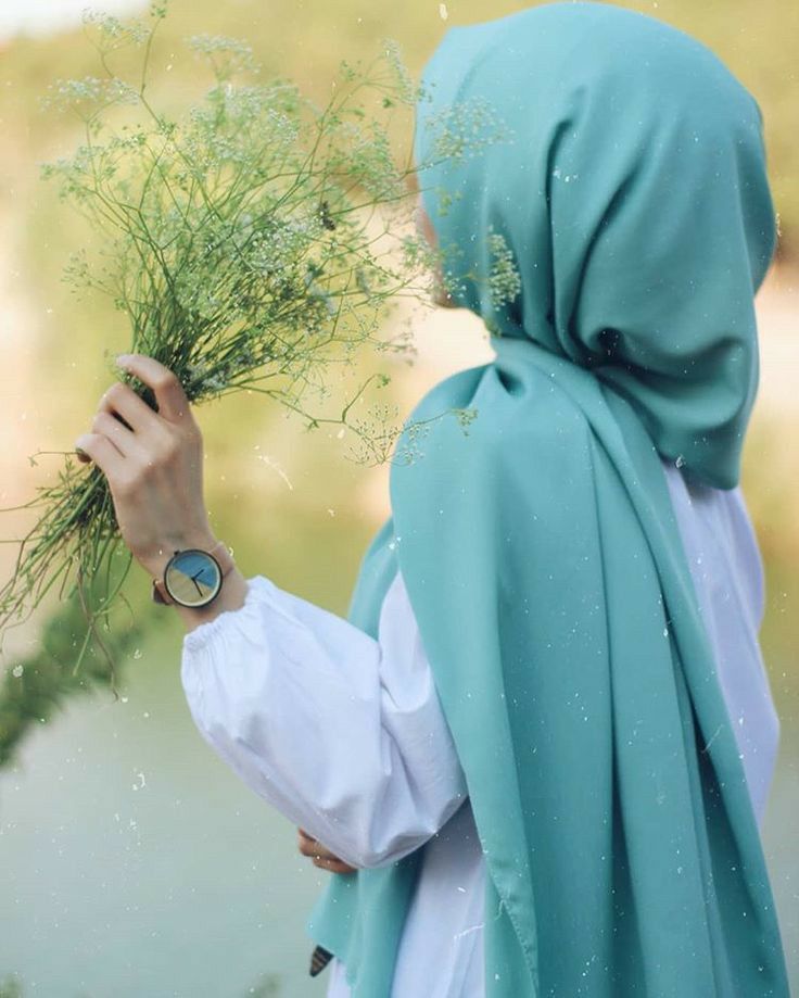 a woman in a blue hijab holding some green plants and looking at the ground