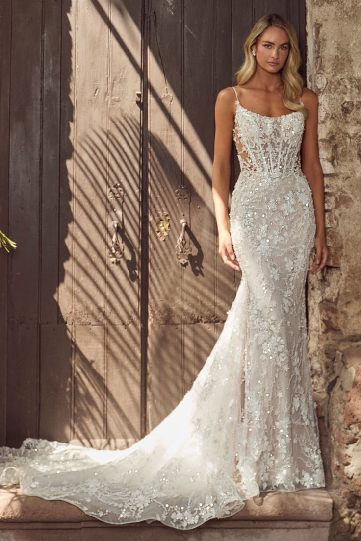 a woman standing in front of a wooden door wearing a wedding dress with an open back