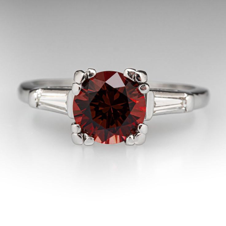 This lovely vintage ring is centered with one (1) round brilliant cut natural rhodolite garnet set into a four-prong setting. The shoulders of the ring are each accented with one (1) channel set, tapered baguette cut diamond. The ring measures 7.6mm at the top, rises 8.1mm above the finger, tapering to 1.2mm wide and 1.1mm thick at the base of the shank. It is currently a size 6.25. Classic Ruby Ring With Polished Round Stone, Classic Ruby Ring With Prong Setting In Platinum, Elegant Ruby Ring With Round Accent Stones, Classic Platinum Ruby Ring With Prong Setting, Elegant Ruby Ring With Accent Stones, Classic Platinum Ruby Ring With Center Stone, Classic Platinum Ruby Ring With Brilliant Cut, Classic Ruby Ring With Round Stone For Formal Occasions, Classic Red Diamond Ring In Platinum