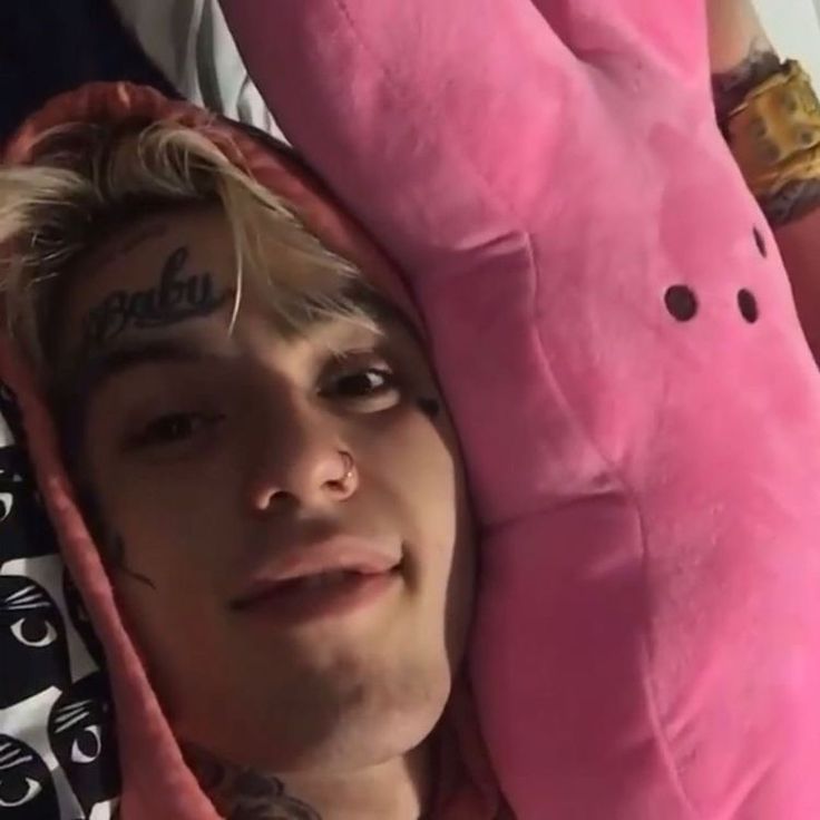 a young man laying in bed next to a pink stuffed animal