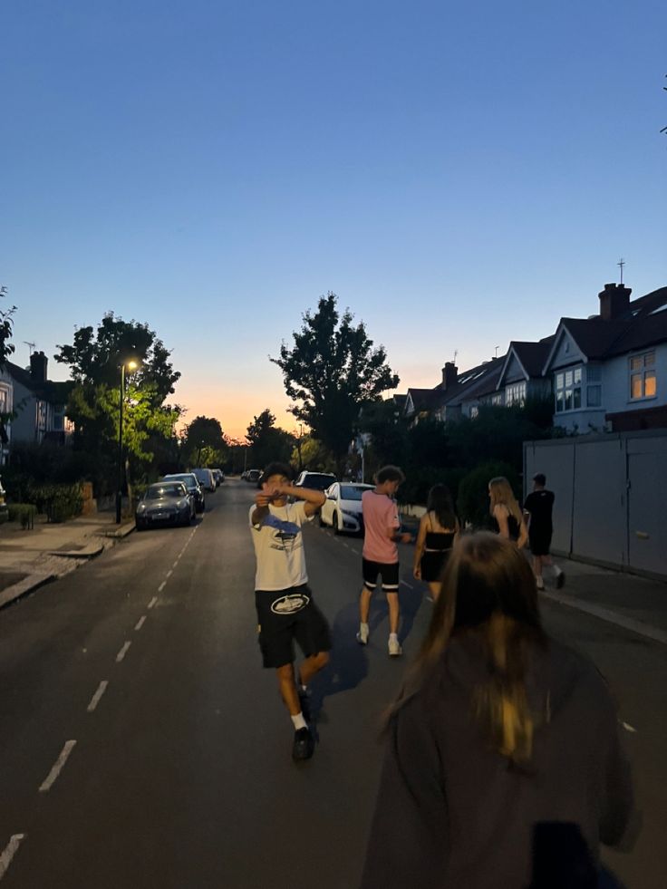 a group of people riding skateboards down a street next to tall buildings at dusk