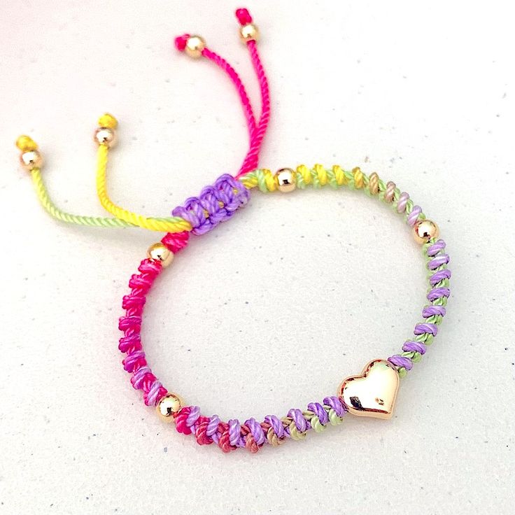 two colorful bracelets with gold hearts and beads on white table top next to each other