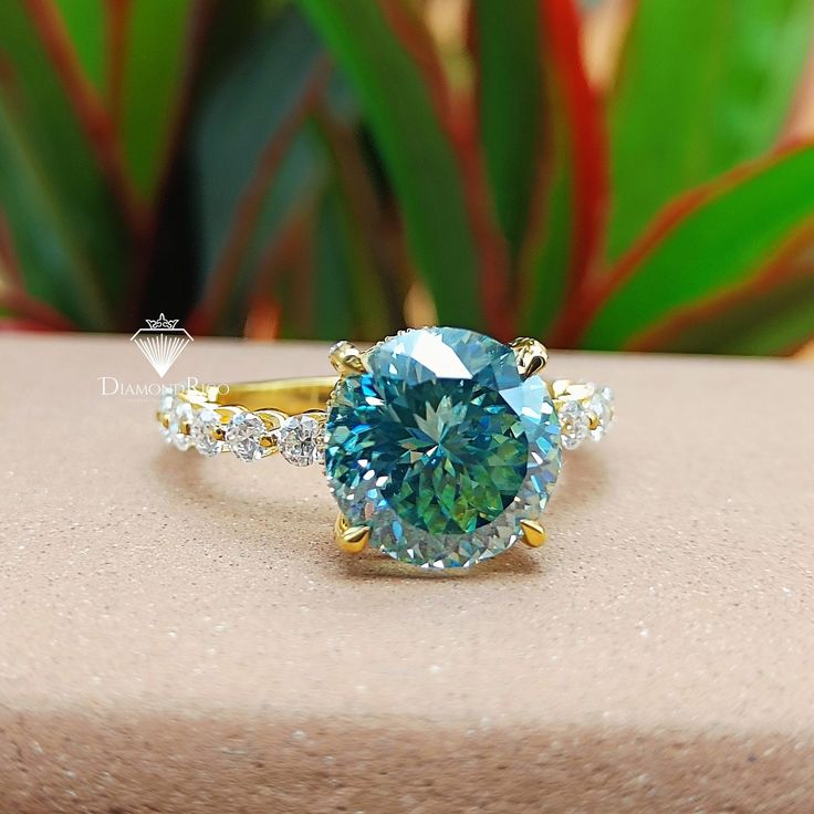 a blue diamond ring sitting on top of a table next to a potted plant