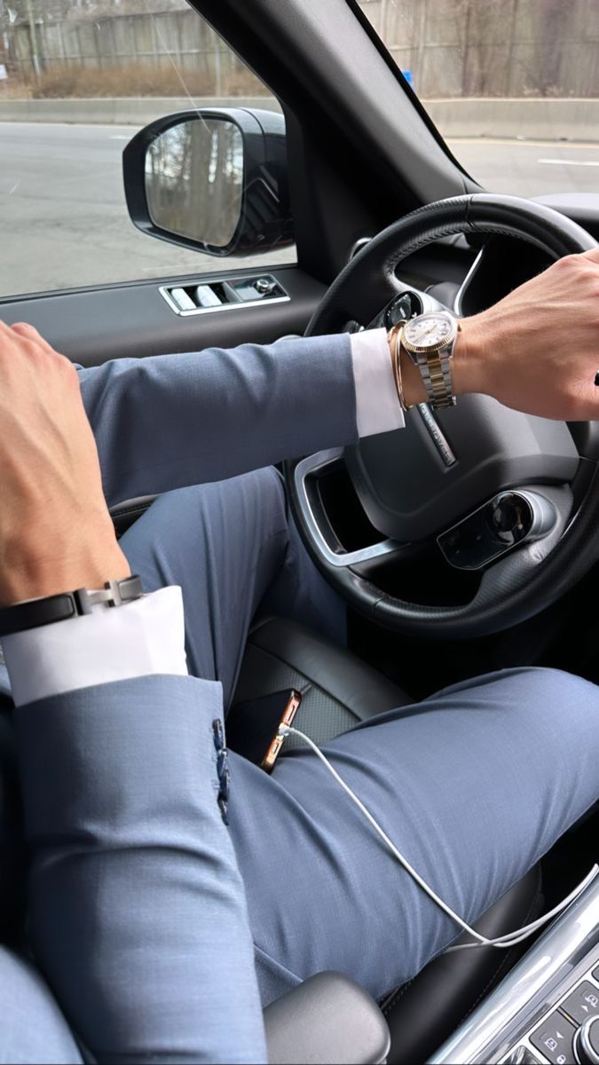 a man in a blue suit driving a car with his hands on the steering wheel