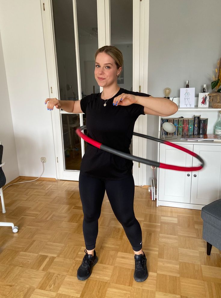 a woman in black shirt and leggings playing with a red hula hoop