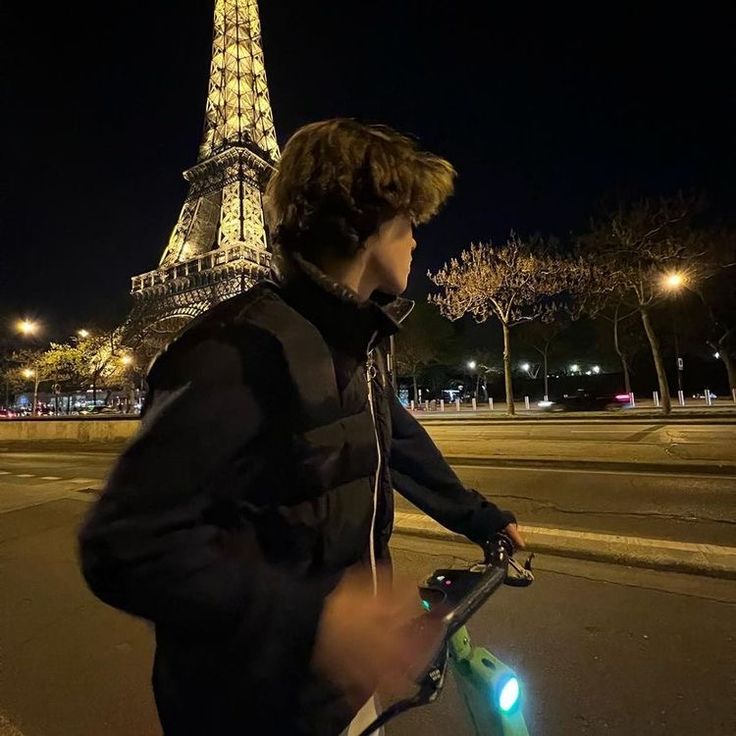 a young man riding his bike in front of the eiffel tower at night