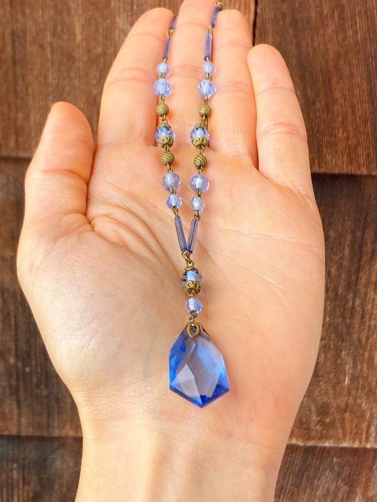 The loop of the clasp on this necklace is marked, 'Czechoslovakia' and it feels old and well made when held. The glass is a periwinkle blue and there is a faceted teardrop pendant at the bottom with a decorative metal top. The beads on the strand are both small and round, and long and cylindrical. There are also small, spherical, gold toned beads with a swirled texture. There is some corrosion around the clasp and a small chip on the pendant. The necklace is being sold As Is for this reason. It Vintage Beaded Jewelry With Czech Glass, Vintage Blue Single Strand Necklace, Vintage Necklace With Polished Beads, Vintage Czech Glass Beaded Necklaces With Polished Beads, Vintage Czech Glass Necklaces With Polished Beads, Antique Single Strand Beaded Necklace Gift, Vintage Czech Glass Necklace With Polished Beads, Vintage Czech Glass Polished Beads Necklace, Antique Single Strand Beaded Necklace As Gift