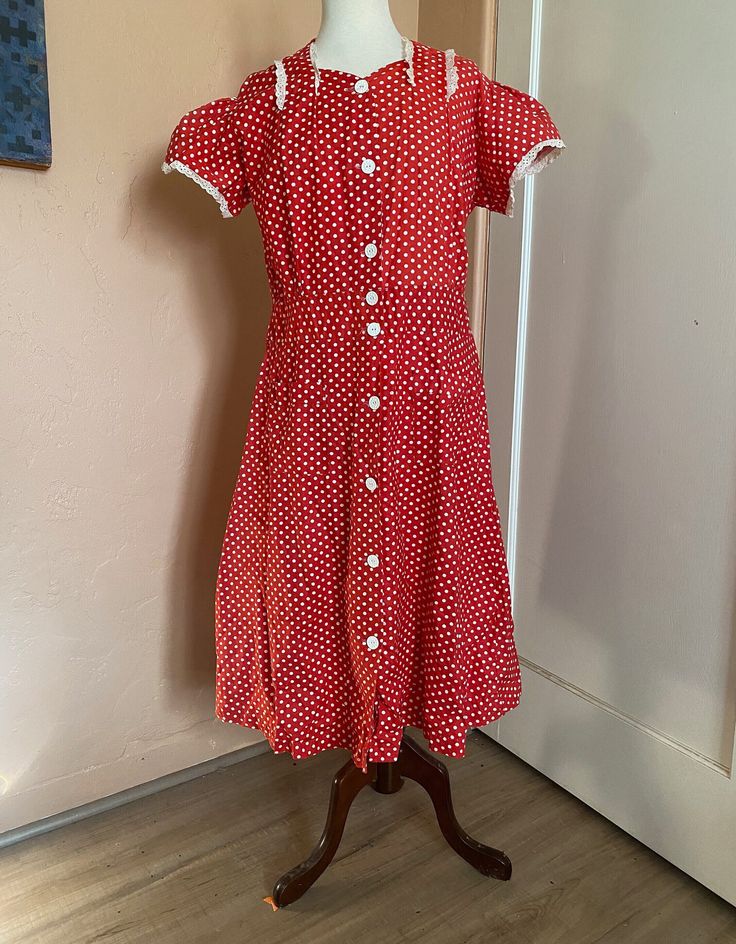 Charming 1940s era short-sleeved, red cotton dress with white polka dots. Abbreviated  sweetheart neckline and short puff sleeves trimmed with delicate, white cotton scalloped and ruffled eyelet trim. Front closure of white plastic buttons that feature an inlaid abstract floral design. Light fading on top of right sleeve (see photo). Researchers: this dress has loads of label info! Front of label reads "Pepsi=Coat Reg. Pend. Guaranteed Washable" - reverse side "Suburban Cottons, Inc." measurements: (taken flat and doubled and measured in inches) estimated size: L - XL bust: 44-45 inches waist: 36 inches hips: 46 inches shoulders: 16.5 inches shoulder to waist: 15 inches length: 42 inches size if marked: remnants of size tag, but unreadable To ensure a good fit, please compare measurements 1950s Style Vintage Dress With Short Sleeves, 1950s Style Fitted Vintage Dress With Short Sleeves, 1950s Short Sleeve Dress For Vintage Fashion, 1950s Short Sleeve Vintage Fashion Dress, 1950s Style Short Sleeve Vintage Dress, 1950s Style Vintage Fashion Dress With Short Sleeves, 1950s Style Short Sleeve Day Dresses, 1950s Style Short Sleeve Dresses For Daywear, Polka Dot Short Sleeve Dress For Daywear