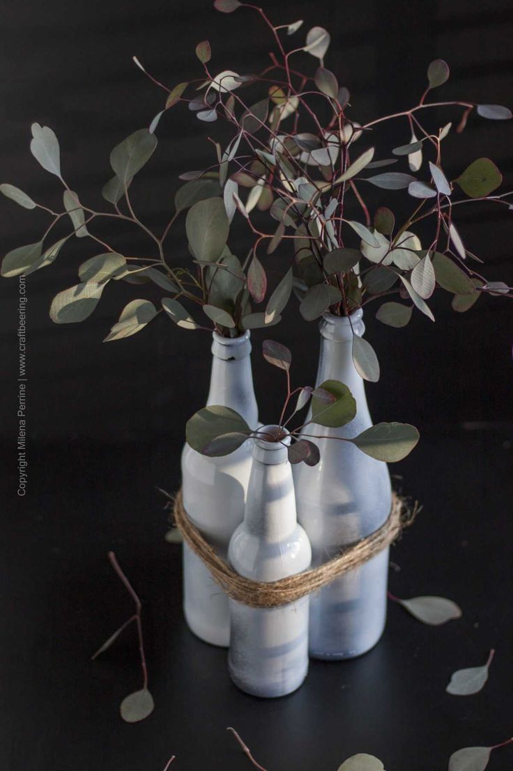 three white vases with plants in them on a black tableclothed surface and scattered leaves