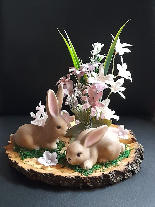 two bunny figurines sitting on top of a piece of wood with flowers in it