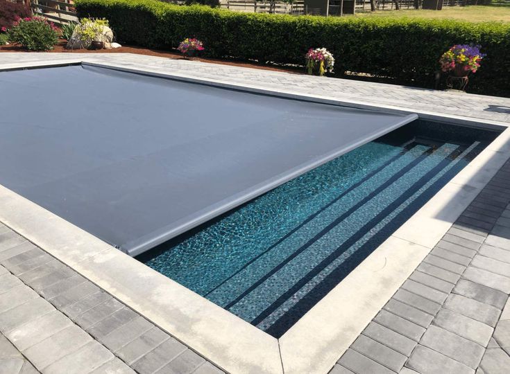 an empty swimming pool in the middle of a brick patio with flowers and shrubs around it