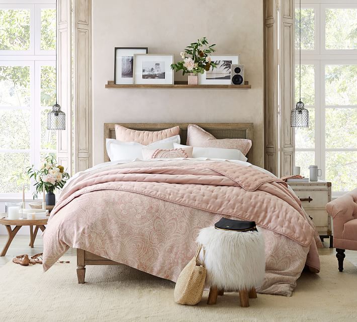 a bedroom with pink bedding and white carpeted flooring in front of large windows