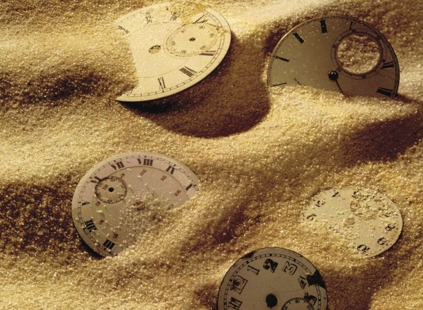 four different clocks sitting on top of sand