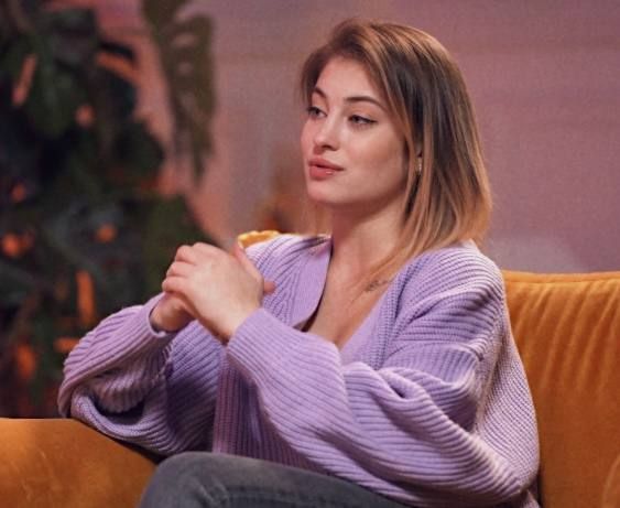 a woman sitting on top of a couch with her hands clasped to her chest and looking off into the distance