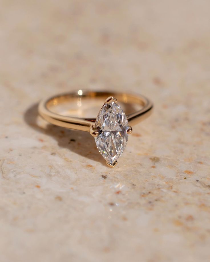 a diamond ring sitting on top of a marble counter next to a gold band that has two pear shaped diamonds in it