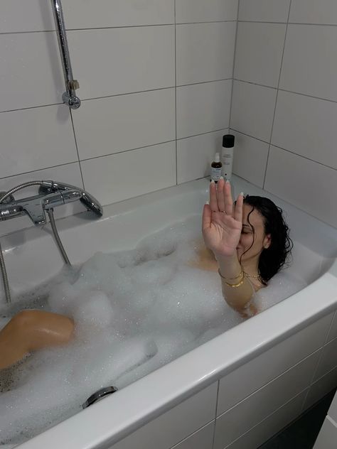 a woman sitting in a bathtub with foam on the floor and her hand out