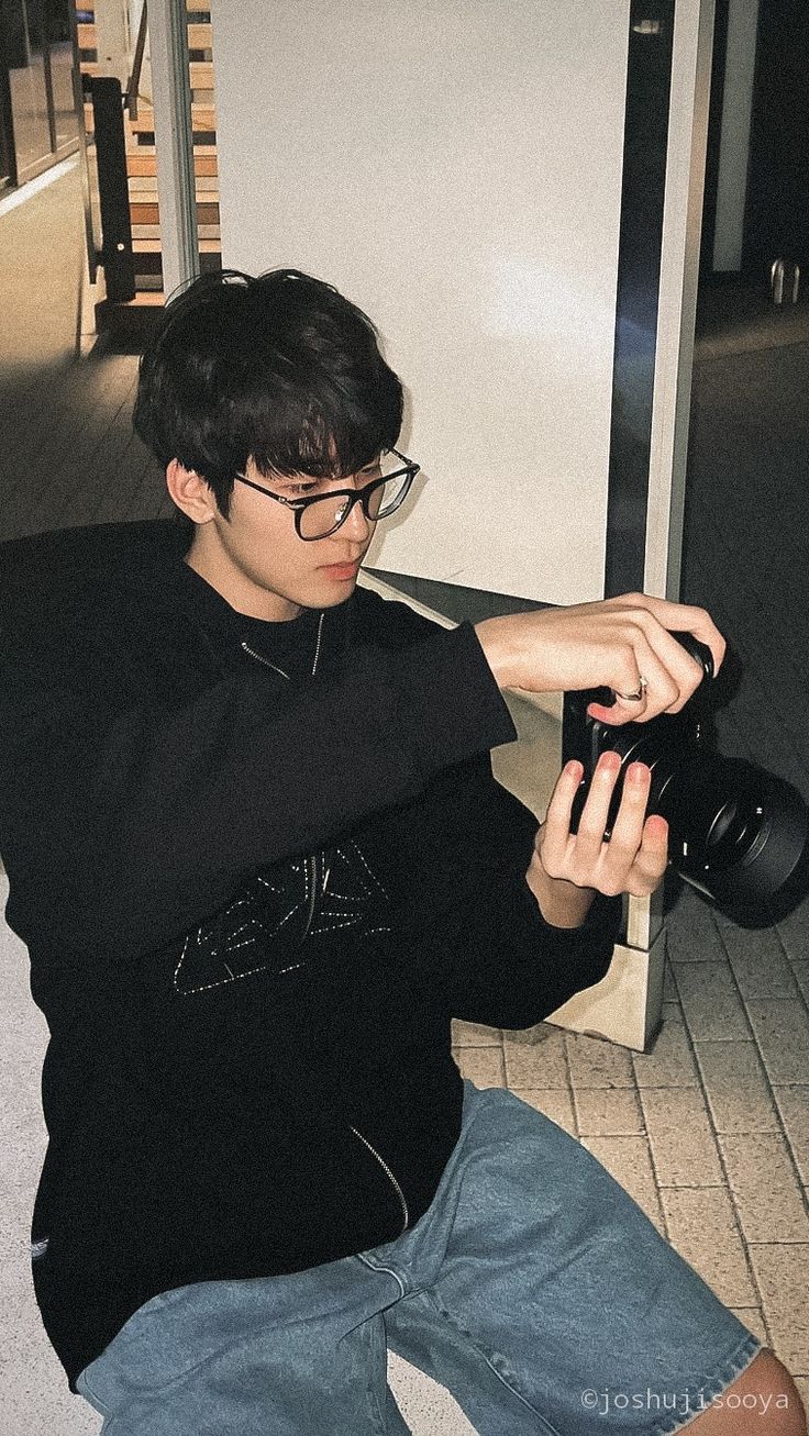 a young man sitting on the floor with a camera in his hand and looking at it