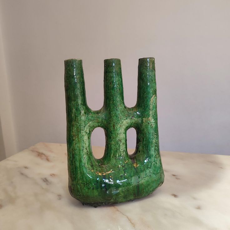 a green vase sitting on top of a white counter next to a black object with holes in it