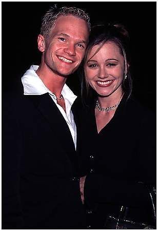 a man and woman standing next to each other in front of a dark background smiling for the camera